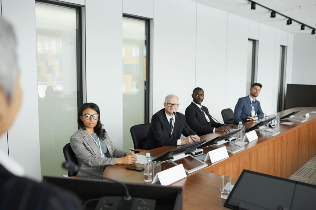 A diverse group of professionals in a modern office setting, seated around a conference table during a business meeting.