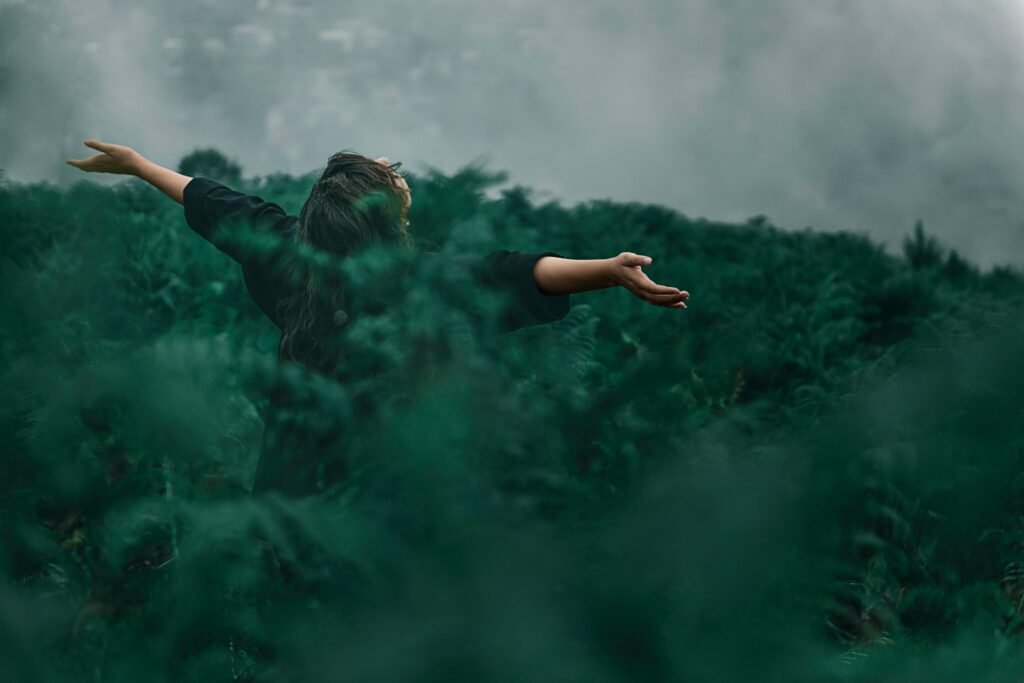 A woman with open arms enjoying freedom in a foggy green landscape.