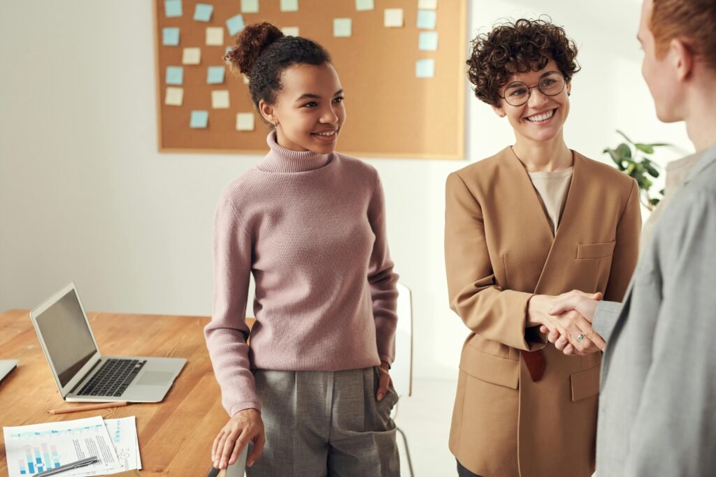 Business colleagues in an office shaking hands and smiling, showcasing teamwork and collaboration.