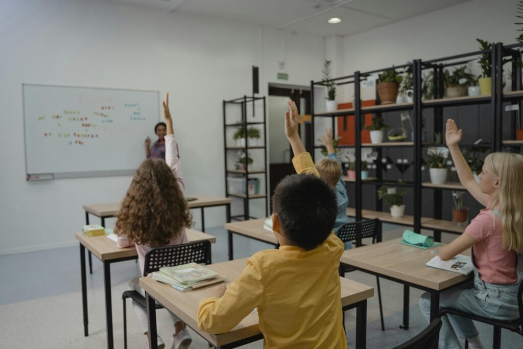 Diverse group of students raising hands in a vibrant classroom setting with teacher at front.