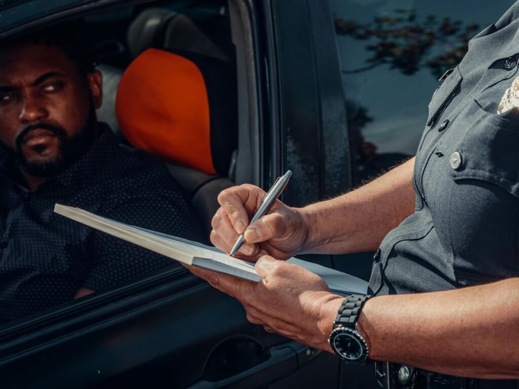 A police officer writes a ticket as the driver looks on from inside the car.